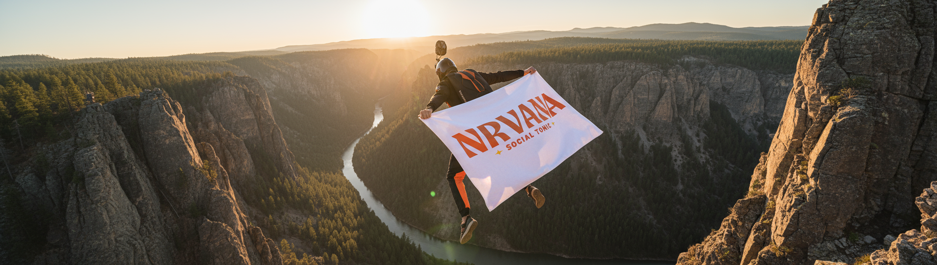 Extreme athlete base jumping over canyon at sunrise holding NRVANA Social Tonic banner above river valley.